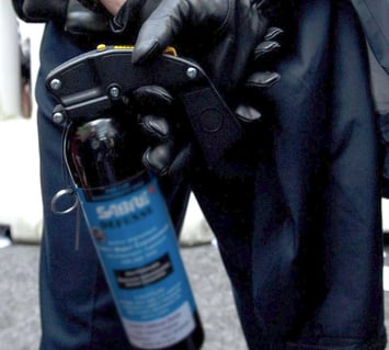 In this image, a police officer holds a gas pepper can while being monitored by a system for asset tracking.