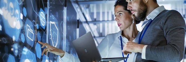A male and female security professional analyzing a digital interface with futuristic icons, highlighting the importance of integrated security technologies in combating cyber-physical threats.
