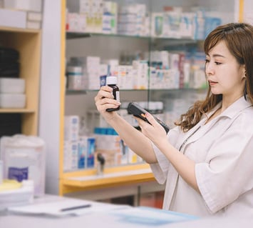 Pharmacist scanning medication bottles with RFID barcode scanner for inventory management.