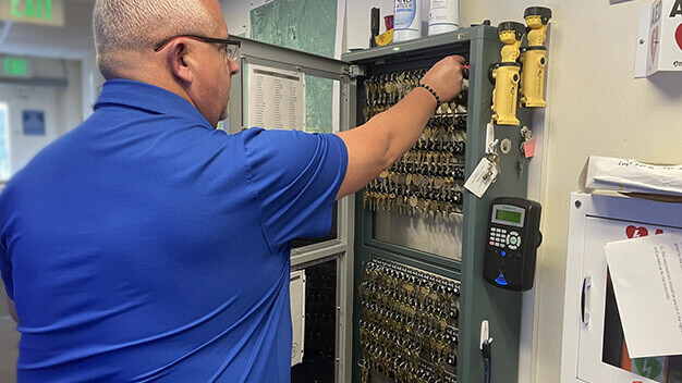 Authorized staff retrieving keys from electronic key management system in school facility - facility access, key security solution, controlled key access